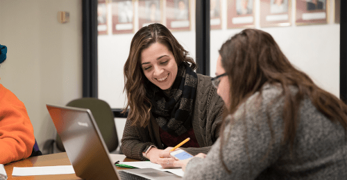 Two happy female students working on one laptop